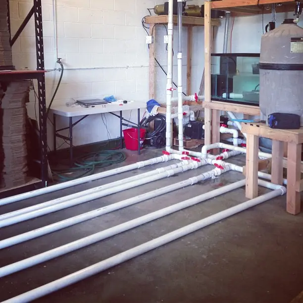 White PVC test manifold, filter tank and glass tank on shelving in the Vacless workshop